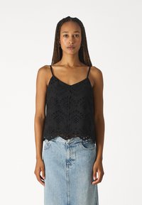 Top noir sans manches avec des découpes en dentelle, un ourlet festonné et des bretelles fines, associé à une jupe en denim bleu clair.