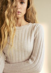 Beige ribbet sweater med lange ærmer, der har en rund halsudskæring og et blødt, struktureret stof, der fremhæver lodrette linjer over hele tøjet.