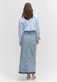 Vaaleansininen farkku-maxihame, jossa on suora leikkaus, kulunut helma ja takataskut. Yhdistetty pitkähiharaiseen siniseen paitaan ja valkoisiin korkokenkiin.