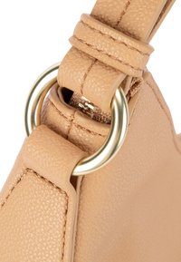 Torba iz rjave usnja z teksturirano površino, z zlatim kovinskim obročem in paščkom z zaponko. Prikaz bližnjega posnetka pritrdilnih elementov.