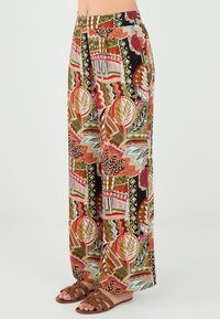 Pantalons larges en tissu coloré et à motifs avec des tons terreux, des formes géométriques et des motifs floraux. Texture douce et taille élastique.
