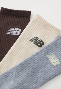 Kolme paari ribadega sokke tumepruunis, kreemis ja helesinis, millest igaühel on New Balance'i logo kontrastsetes värvides.