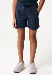 Shorts de color azul marino con cinturilla elástica y cordón, que cuentan con bolsillos laterales y dobladillo recto. Llevados con zapatillas de color púrpura claro.
