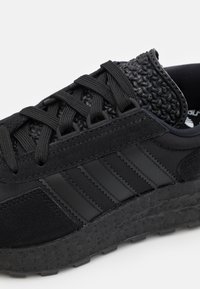 Svart atletisk sko med en texturerad syntetisk ovandel, släta läderdetaljer, tre sidostriper och en gummisula med ett mönstrat mönster.