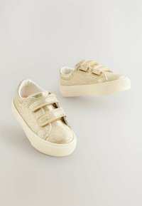 Des baskets dorées pailletées avec une texture lisse, dotées de deux lanières Velcro, d'un bout arrondi et d'une semelle en caoutchouc de couleur claire.