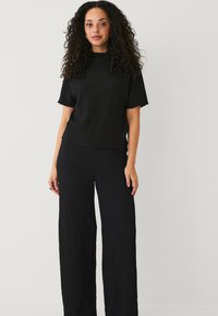 Zwart gemêleerd gebreid outfit met een relaxed-fit top met korte mouwen en een broek met wijde pijpen, beide met een gekreukeld effect.