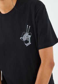 Svart bomullströja med ett vitt grafikmotiv av en takeout-låda med nudlar och ätpinnar, märkt med "Yokohama Chinatown" under.