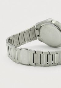 Nerūdijančio plieno laikrodis su susietos apyrankės dizainu, pasižymintis lygia, matinio paviršiaus apdaila ir poliruotu rėmeliu. Užsegime pažymėta "TIMEX".