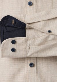 Beige geruite shirtmanchet met zwarte knopen en contrasterende donkere binnenstof, met twee knoopgaten en twee gestikte knopen.