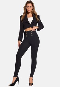 Czarna krótka marynarka na jeden guzik, zestawiona z wysokim stanem czarnych spodni z złotymi guzikami i dopasowanym krojem. Czarne szpilki.