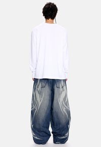 Λευκό πουκάμισο με μακριά μανίκια σε συνδυασμό με φαρδιά μπλε τζιν τζιν με γκρι φλόγα στο κάτω μέρος των ποδιών και άνετη εφαρμογή.