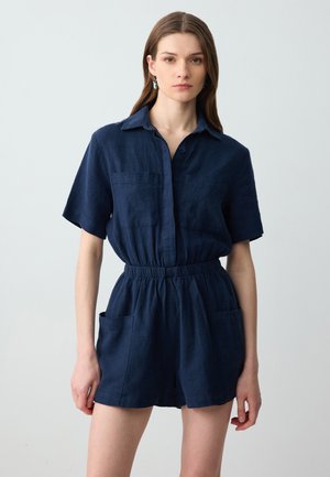 Overall in lino blu navy con maniche corte, chiusura frontale con bottoni, vita elastica e due tasche anteriori. Texture liscia, design casual.