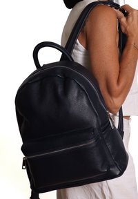 Zaino in pelle blu navy con forma arrotondata, superficie texturizzata, spallacci regolabili e una tasca frontale con zip. Progettato per un uso quotidiano.