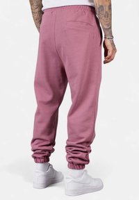 Cotton joggers in muted pink with elastic cuffs, a back pocket, and a soft texture, paired with white sneakers.