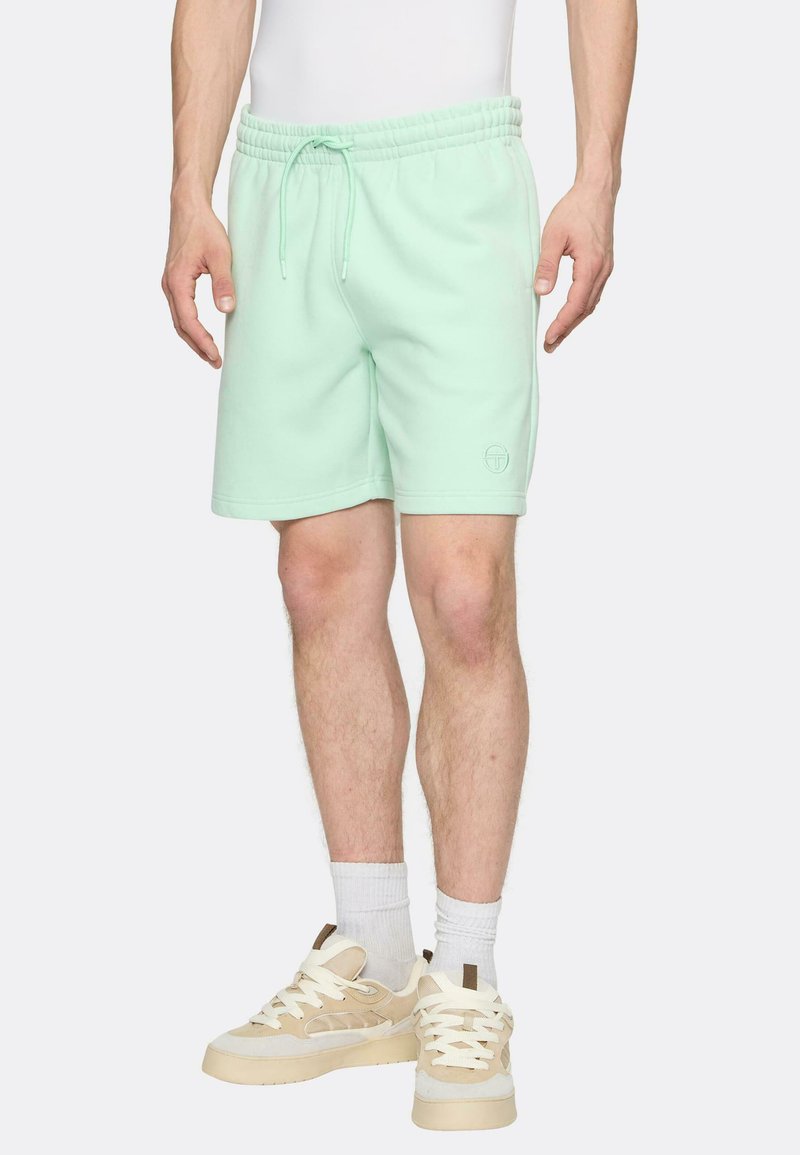 Bavlněné šortky v barvě mátově zelené s elastickým pasem a šňůrkou. Na nohavici je jemný detail s logem. Kombinovány s béžovými teniskami.