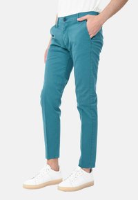 Chinos in cotone turchese, slim fit, davanti piatto, con tasche laterali e chiusura a pulsante. Abbinati a sneaker bianche con suola beige.