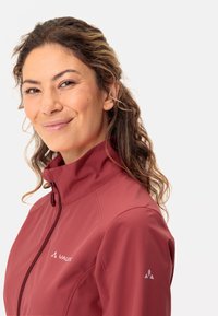 Giacca softshell rossa con colletto alto, chiusura a zip frontale e dettagli con logo sul petto e sulla manica; tessuto leggero e dalla texture liscia.