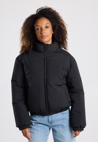 Giacca a vento nera con colletto alto, chiusura con zip e polsini elasticizzati. Presenta un design corto e una superficie liscia e lucida.