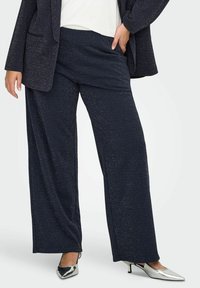 Morske široke hlače iz teksturirane tkanine s diskretnimi metalnimi delci, v kombinaciji s srebrnimi čevlji z ostrim koncem.