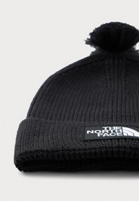Svart ribbestrikket lue med pom-pom og brettet oppkant, med The North Face-logo i svart og hvitt.