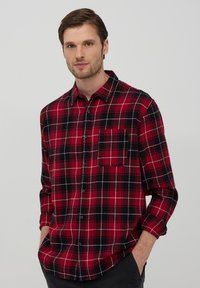 Camicia a quadri rossa e nera in tessuto flanella, con taschino sul petto e maniche lunghe con polsini abbottonati.