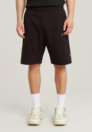Sorte bomulds-shorts i en afslappet pasform med sidelommer, et lille blåt logo-patch og en stikning på kanten.