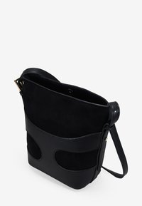 Bolso cruzado de ante y cuero negro con una forma estructurada, que presenta detalles troquelados y una sola correa ajustable.