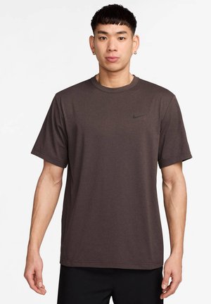 Tricou scurt cu mânecă, de culoare maro închis, cu decolteu rotund și logo-ul Nike negru pe piept. Material ușor, cu o textură netedă.