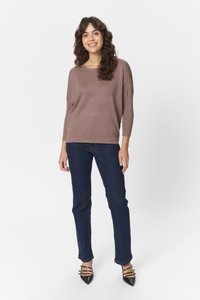 Barna kötött pulóver ¾-es ujjal, sötétkék, slim-fit farmernadrággal és fekete hegyes orrú magassarkú cipővel, díszes pántokkal párosítva.