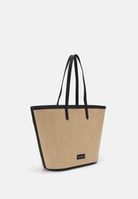 Sac fourre-tout beige tissé avec bordure noire et poignées, forme rectangulaire, et petite étiquette rectangulaire avec logo au centre devant.