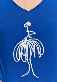 Top azul con escote en V y un dibujo lineal blanco de una figura estilizada con vestido. La tela parece suave con una textura lisa.