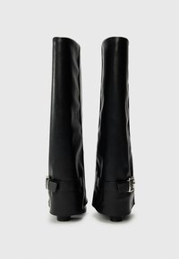 Bottes noires montantes en cuir lisse, avec un accent de boucle au niveau de la cheville et un design élancé légèrement effilé.