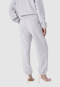 Graue Jogginghosen mit elastischem Bund, tapered Knöcheln und weicher Textur, kombiniert mit weißen High-Heel-Sandalen, von hinten betrachtet.