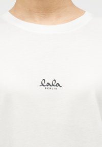 Λευκό βαμβακερό t-shirt με στρογγυλή λαιμόκοψη. Διαθέτει μικρό, μαύρο λογότυπο «lala BERLIN» στο στήθος. Λείο ύφασμα και απλός σχεδιασμός.