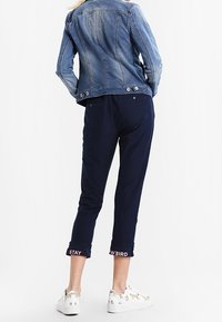 Dżinsowa kurtka z odcieniem wyblakłym, granatowe spodnie w kroju 7/8 z napisem "BĄDŹ DZIWNY" na mankietach oraz wzorzyste białe trampki.