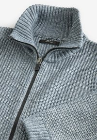 Grauer gestrickter Reißverschluss-Pullover mit hohem Rippenkragen und kontrastierendem Reißverschluss. Verfügt über ein strukturiertes Muster und ein Markenlabel am Kragen.