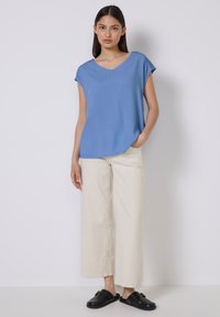 Blusa blu a maniche corte con scollatura a V, abbinata a pantaloni ampi color crema e sandali neri a scivolo. Tessuto morbido con vestibilità rilassata.