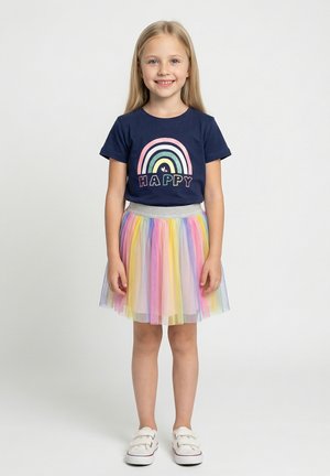 Marineblaues Baumwoll-T-Shirt mit Regenbogengrafik und dem Schriftzug "HAPPY", kombiniert mit einem mehrfarbigen Tüllrock. Weiße Slip-On-Schuhe.