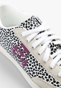 Sneaker z plisowanym czarno-białym wierzchem, beżowymi panelami z zamszu, białymi sznurowadłami i fioletowym wzorem czaszki po boku.