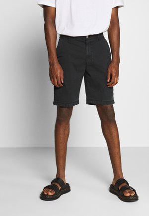 Svarta bomullshorts med rak skärning, framfickor och en enda knäppning, i kombination med svarta sandaler med tjocka remmar.