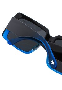 Musta aurinkolasit sinisin yksityiskohdin, joissa on geometrinen muotoilu ja leveät linssit. Kehys on kiiltävä ja siinä on tukeva saranarakenne.