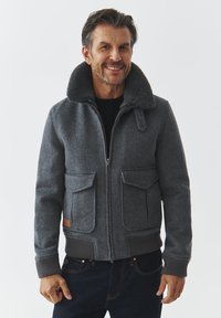 Giacca di lana grigia con colletto in pelliccia, zip frontale e due tasche con pattina. Presenta polsini e orlo a costine, con dettaglio in pelle sul lato.