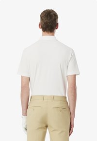 Hvid polo-shirt med korte ærmer og krave, parret med beige bukser der har baglommer og knapdetaljer.