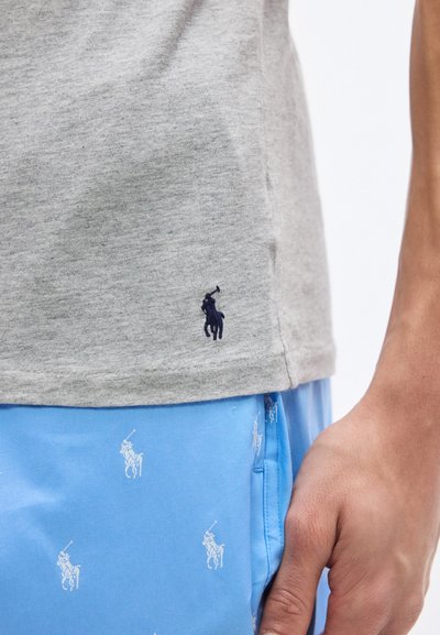 Κοντινό πλάνο ενός ατόμου που φοράει γκρι πουκάμισο με λογότυπο ποδοσφαιριστή πόλο σε ναυτικό μπλε και ανοιχτόχρωμο μπλε σορτς με σχέδιο από μικρά λευκά λογότυπα ποδοσφαιριστή πόλο.