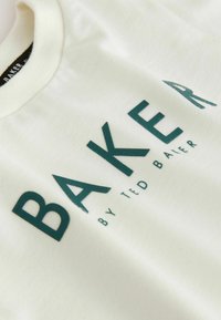 Camiseta de algodón crema con lettering en un atrevido tono verde azulado que dice "BAKER" y "by TED BAKER" debajo, con cuello redondo y textura suave.