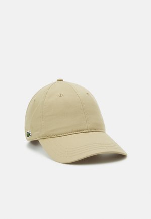 Casquette de baseball beige en coton avec une visière incurvée et un petit logo crocodile vert sur le côté, présentée sur un fond uni clair.