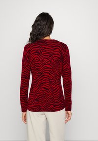 Pull rouge à manches longues avec un motif zèbre noir, un col côtelé et une finition texturée, vu de dos.