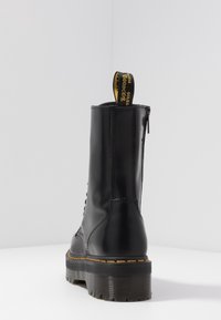Bota de tobillo de cuero negro con suela texturizada, diseño con cordones y costuras amarillas en contraste. Cuenta con una lengüeta para facilitar su colocación.