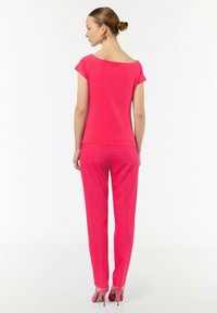 Fuksjowa bluzka z szerokim dekoltem i krótkimi rękawami w zestawie z dopasowanymi spodniami. Buty mają różowy akcent i wysokie obcasy. Gładka, miękka tekstura.