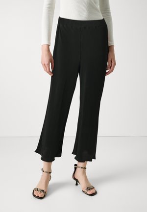 Pantalons larges plissés noirs avec une taille lisse, confectionnés dans un tissu léger et d'une longueur cropped, associés à des sandales à talons avec lanières.